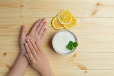Young woman applying natural lemon scrub on hands against wooden table